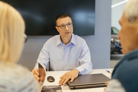 Salesperson advising couple in car dealership stock photo