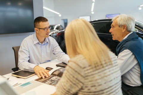 Verkäufer, der ein Paar im Autohaus berät, lizenzfreies Stockfoto