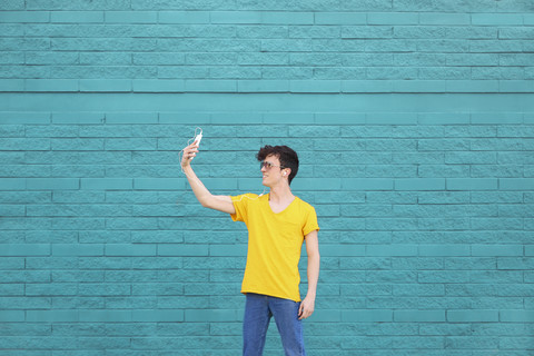 Young man taking a selfie with smartphone in front of blue brick wall stock photo