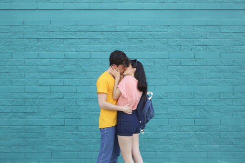 Young couple kissing in front of blue brick wall - RTBF00911