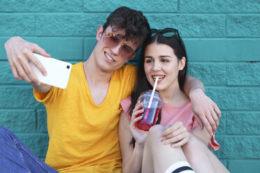 Young couple taking selfie with smartphone in front of blue brick wall - RTBF00916