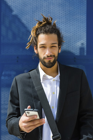 Porträt eines jungen Geschäftsmannes mit Dreadlocks, der ein Smartphone benutzt, lizenzfreies Stockfoto