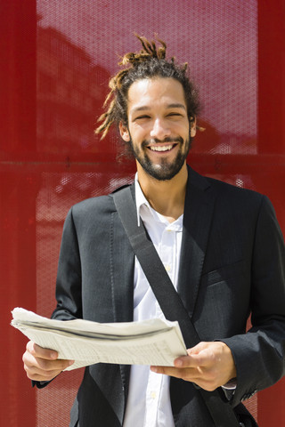 Portrait of young businessman with dreadlocks reading newspaper stock photo