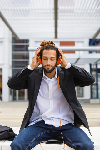 Portrait of young businessman with dreadlocks listening music with headphones and cell phone stock photo