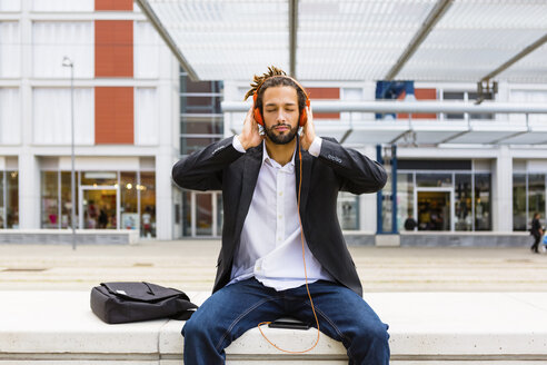 Porträt eines jungen Geschäftsmannes mit Dreadlocks, der mit Kopfhörern und Mobiltelefon Musik hört - MGIF00023