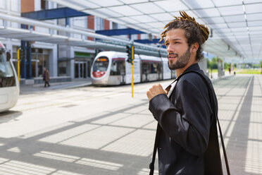 Porträt eines jungen Geschäftsmannes mit Dreadlocks, der am Bahnhof wartet - MGIF00027