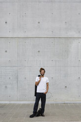 Lächelnder junger Geschäftsmann mit Dreadlocks vor einer Betonwand stehend - MGIF00029