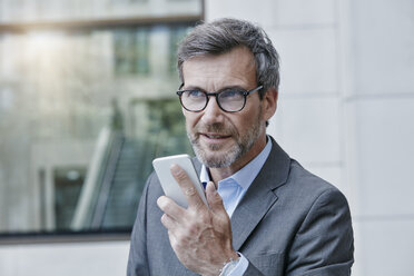 Portrait of businessman speaking voice mails on his smartphone - RORF00975