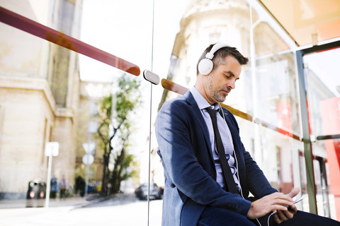 Businessman with smartphone and headphones waiting at the bus stop stock photo