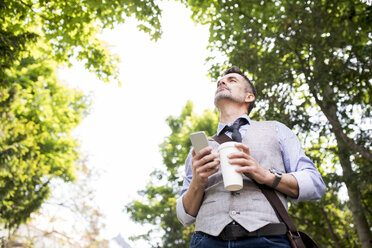 Älterer Geschäftsmann mit Kaffee und Smartphone im Stadtpark - HAPF01756