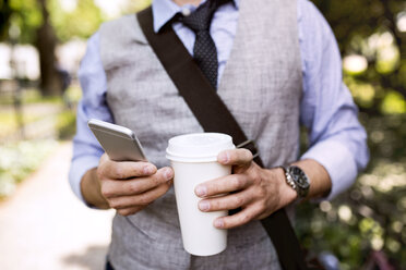 Nahaufnahme eines Geschäftsmannes mit Kaffee und Smartphone im Stadtpark - HAPF01757