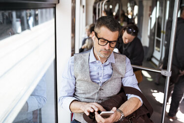 Geschäftsmann mit Smartphone und Kopfhörern in der Straßenbahn - HAPF01764