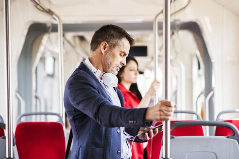 Geschäftsmann mit Smartphone und Kopfhörern auf einer Busfahrt - HAPF01770