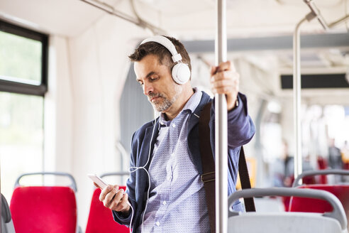 Geschäftsmann mit Smartphone und Kopfhörern auf einer Busfahrt - HAPF01771
