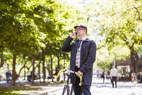 Mature businessman with bicycle and smartphone in the city - HAPF01779