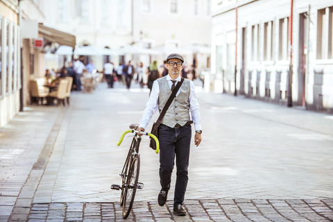 Älterer Geschäftsmann schiebt Fahrrad in der Stadt, lizenzfreies Stockfoto