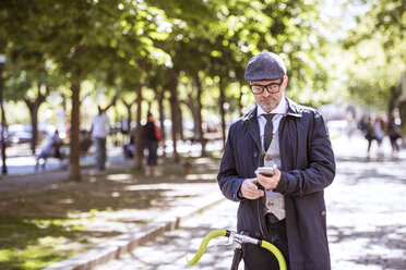 Mature businessman with bicycle and smartphone in the city - HAPF01782