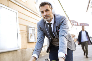 Mature businessman with headphones riding bicycle in the city - HAPF01785