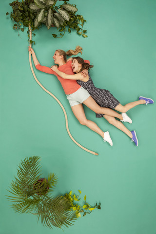 Zwei Frauen schwingen sich an einer Liane durch den Dschungel, lizenzfreies Stockfoto