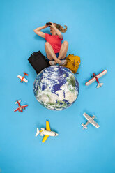 Frau sitzt mit Gepäck auf der Welt und benutzt ein Fernglas - BAEF01515