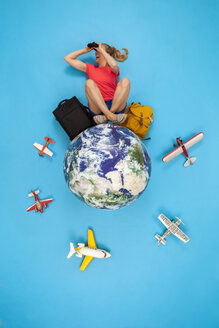 Woman sitting on the world with luggage, using binoculars - BAEF01515