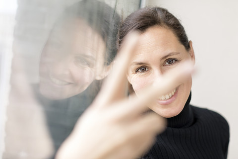 Reflection and portrait of smiling businesswoman showing victory sign stock photo
