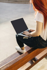 Rothaarige Frau sitzt auf einer Bank und benutzt einen Laptop - JPF00243