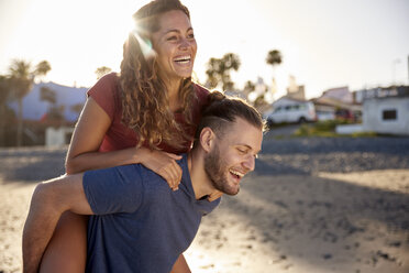 Young man giving his girlfriend a piggyback ride on the beach - PACF00015