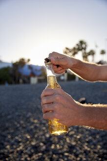 Männerhände öffnen Bierflasche am Strand - PACF00029