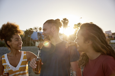 Drei Freunde mit Bierflaschen am Strand bei Sonnenuntergang, lizenzfreies Stockfoto