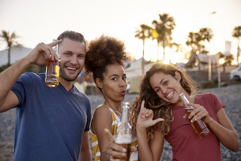 Drei Freunde mit Bierflaschen haben Spaß am Strand bei Sonnenuntergang - PACF00040