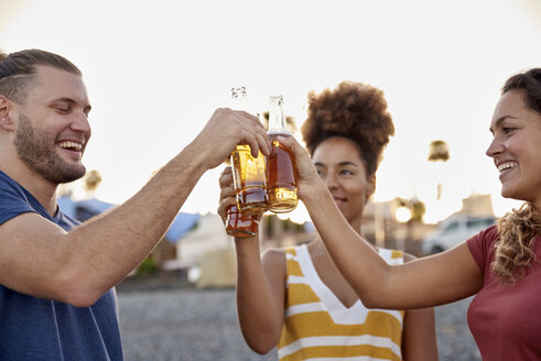 Drei Freunde stoßen mit Bierflaschen am Strand bei Sonnenuntergang an - PACF00041