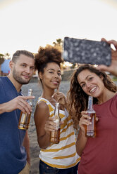 Drei Freunde mit Bierflaschen machen ein Selfie am Strand - PACF00042