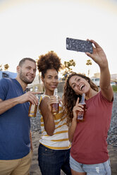 Three friends with beer bottles taking selfie on the beach - PACF00043