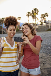 Zwei lachende Freunde mit Bierflaschen machen ein Selfie am Strand - PACF00051