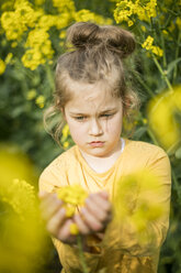 Mädchen begutachtet Pflanze im Rapsfeld - MOEF00012
