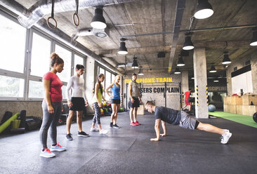 Group of young people watching young man doing push-ups in gym - HAPF01799