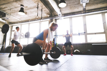 Junge Frau mit Trainingspartnern, die sich darauf vorbereiten, eine Langhantel im Fitnessstudio zu heben - HAPF01814