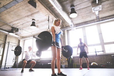 Young woman with training partners lifting barbell in gym - HAPF01815