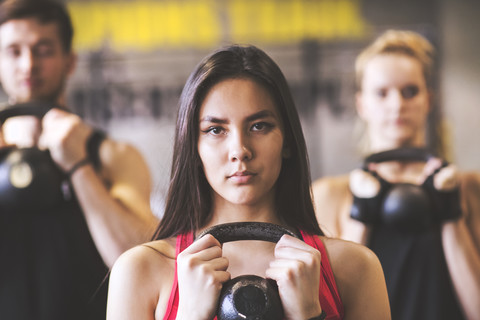 Confident young woman with training partners lifting kettlebell in gym stock photo