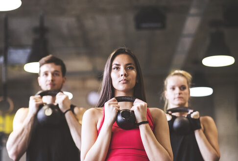 Selbstbewusste junge Frau mit Trainingspartnern, die eine Kettlebell im Fitnessstudio heben - HAPF01834