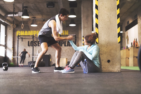 Ein Sportler hilft einer jungen Frau beim Aufstehen nach einer Pause im Fitnessstudio, lizenzfreies Stockfoto