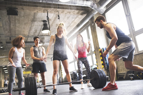 Gruppe junger, fitter Leute, die eine Frau beim Gewichtheben im Fitnessstudio anfeuern - HAPF01839