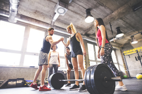 Gruppe junger fitter Leute, die eine Frau beim Gewichtheben im Fitnessstudio motivieren, lizenzfreies Stockfoto