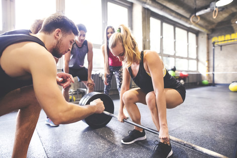 Gruppe junger, fitter Leute, die eine Frau beim Gewichtheben im Fitnessstudio anfeuern, lizenzfreies Stockfoto