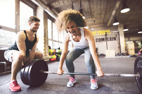 Junge Frau mit Trainingspartner bei der Vorbereitung auf das Heben einer Langhantel im Fitnessstudio, lizenzfreies Stockfoto