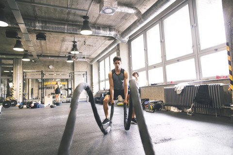 Junger Sportler beim Training mit Seilen im Fitnessstudio, lizenzfreies Stockfoto