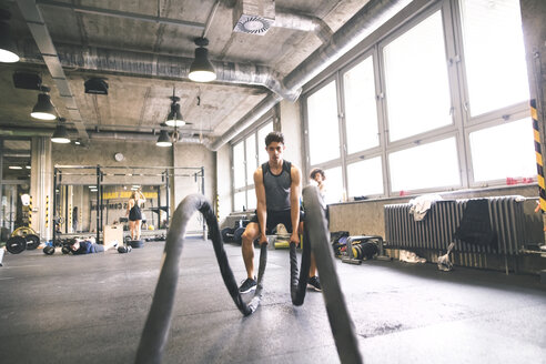 Junger Sportler beim Training mit Seilen im Fitnessstudio - HAPF01855