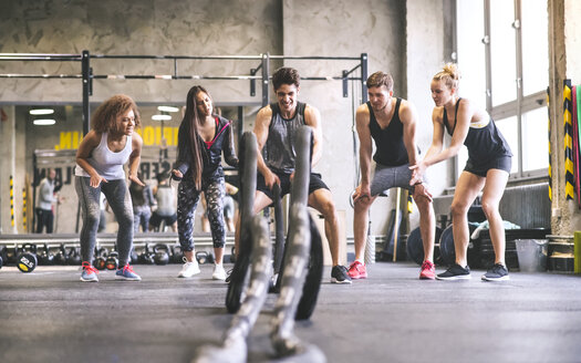 Eine Gruppe junger, fitter Leute jubelt einem Mann zu, der in einem Fitnessstudio mit Seilen trainiert - HAPF01857