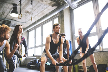 Eine Gruppe junger, fitter Leute jubelt einem Mann zu, der in einem Fitnessstudio mit Seilen trainiert - HAPF01858